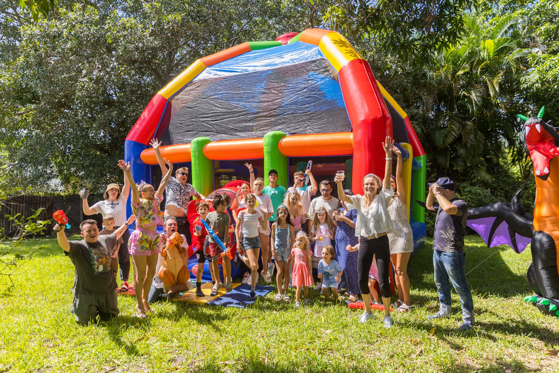 Children and parents cheer with their arms up in front of the bounce house and the giant inflatable dragon